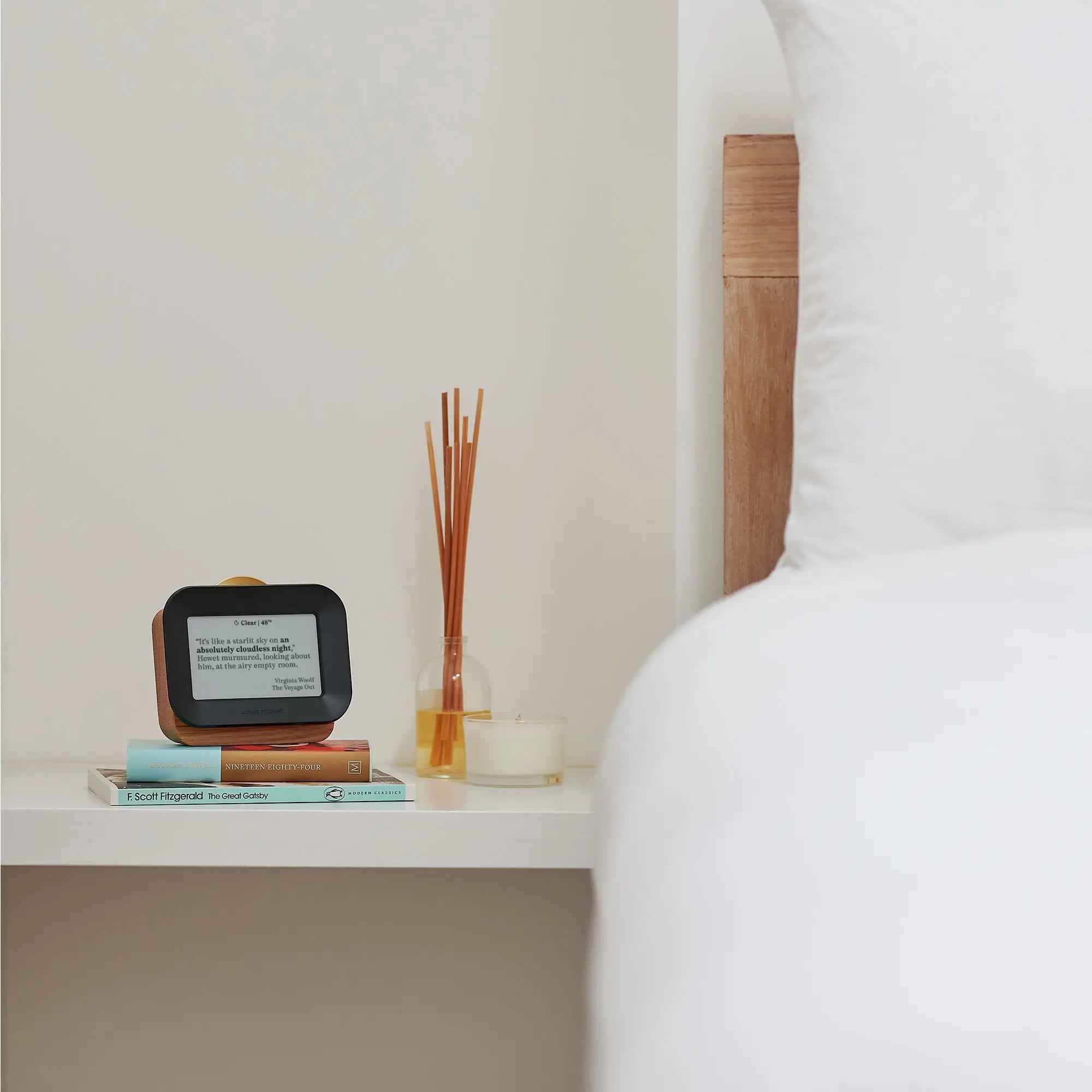 Author Forecast Vol 1 on a bedside shelf displaying a weather quote, styled alongside books, a candle, and a reed diffuser in a calm minimalist bedroom setting.