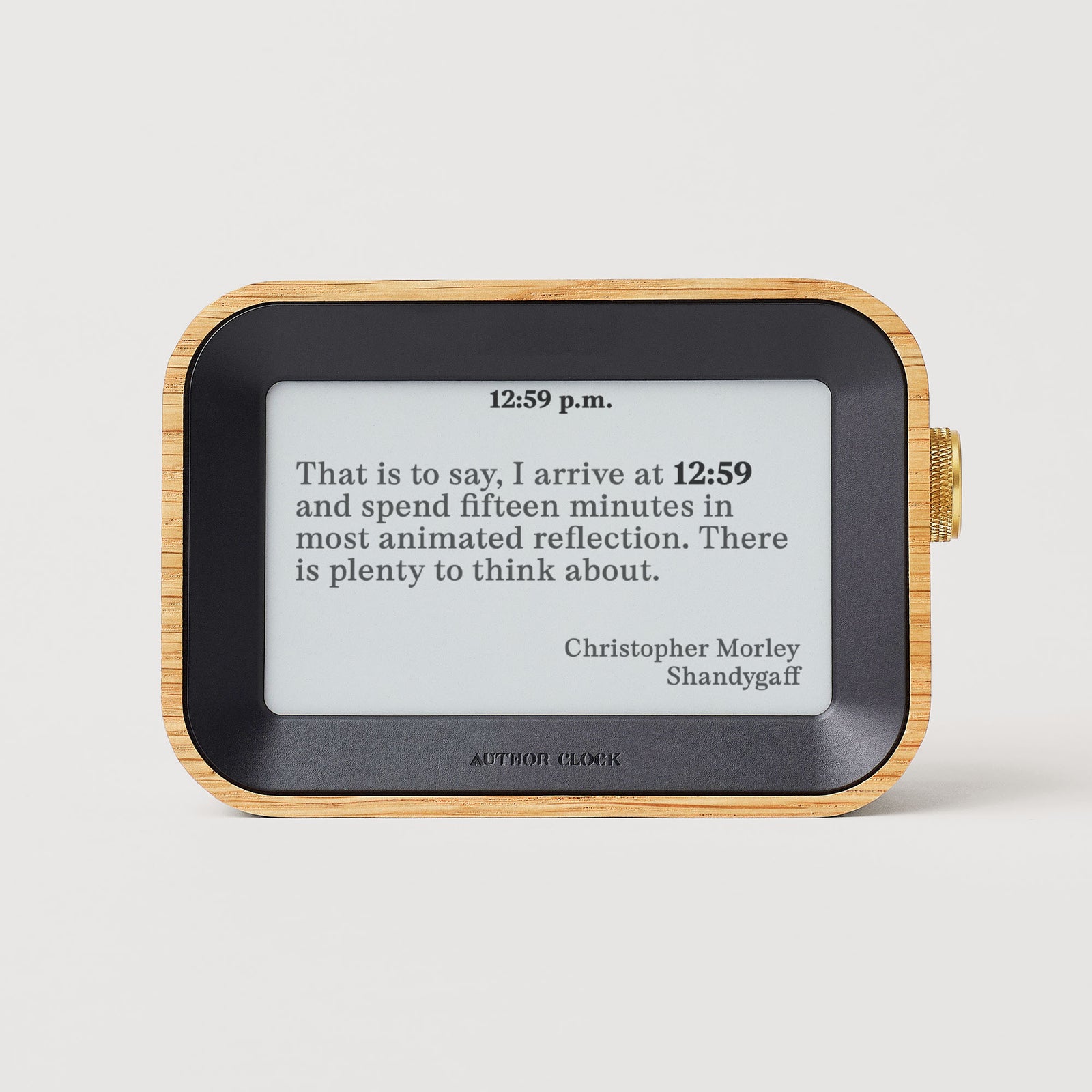 A rectangular wooden-framed digital clock displays "12:59 p.m." above a quote by Christopher Morley.